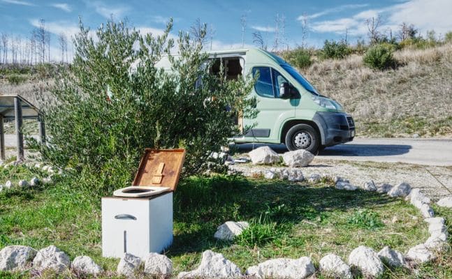 Eine Trockentrenntoilette von Kildwick vor einem Olivenbusch und einem Campervan in Spanien in Szene gesetzt
