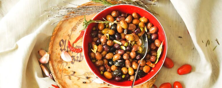 Frisch eingelegte Oliven mit Kräutern, Knoblauch und Chili in einer dekorativen roten Schüssel serviert.